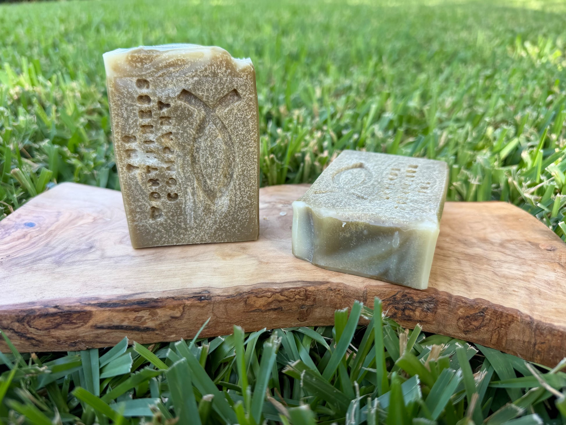 Two handmade rectangular bars of soap with carved Christian fish design displayed on a rustic wooden board.