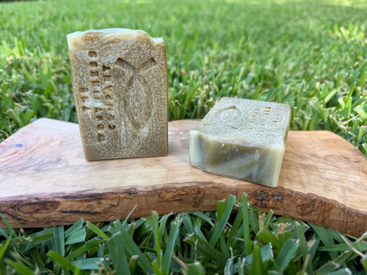Two handmade rectangular bars of soap with carved Christian fish design displayed on a rustic wooden board.