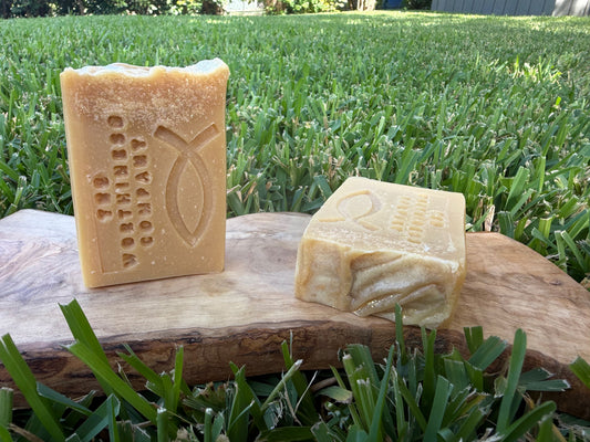 Two rectangular bars of handmade soap displayed on a wooden slab.