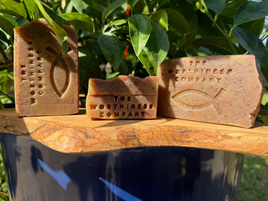 Three rustic bars of handmade soap from The Worthiness Company, displayed on a wooden board.