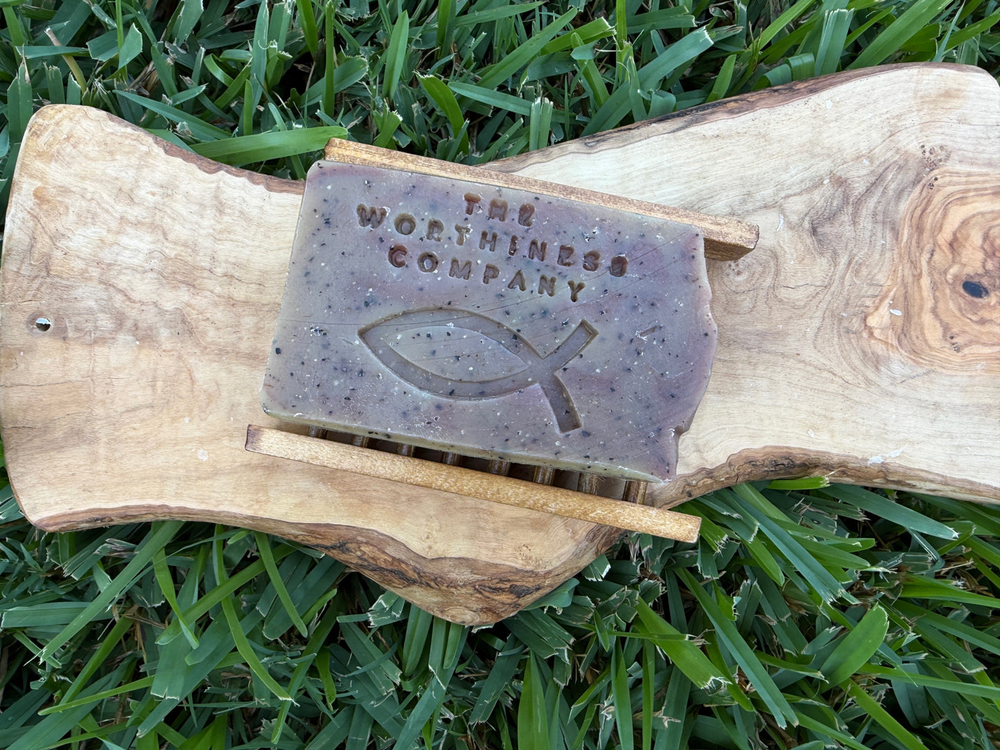 A rectangular bar of soap from The Worthiness Company, embossed with a Christian fish symbol resting on a small soap stand.