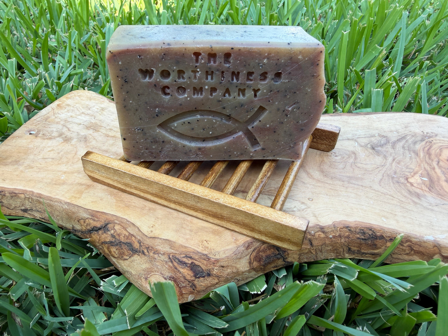 A rectangular bar of soap from The Worthiness Company sits on a small wooden soap dish.