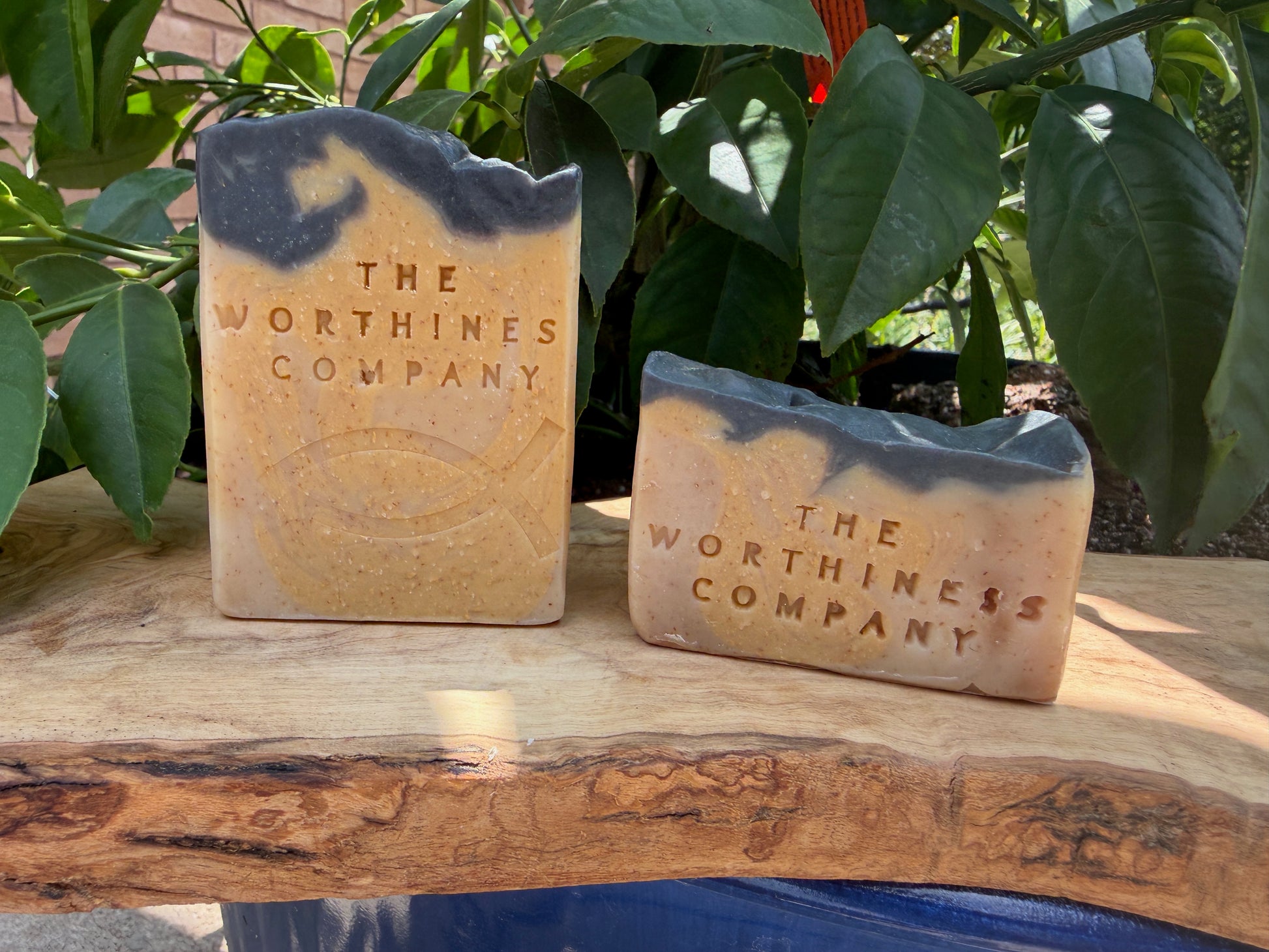 Two rustic decorative stone slabs engraved with 'THE WORTHINESS COMPANY' displayed on a wooden surface.